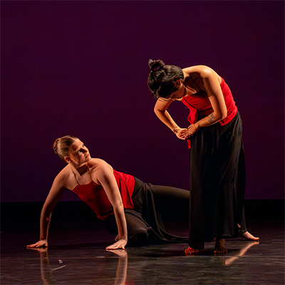 Two contemporary dancers performing on stage in red tops.